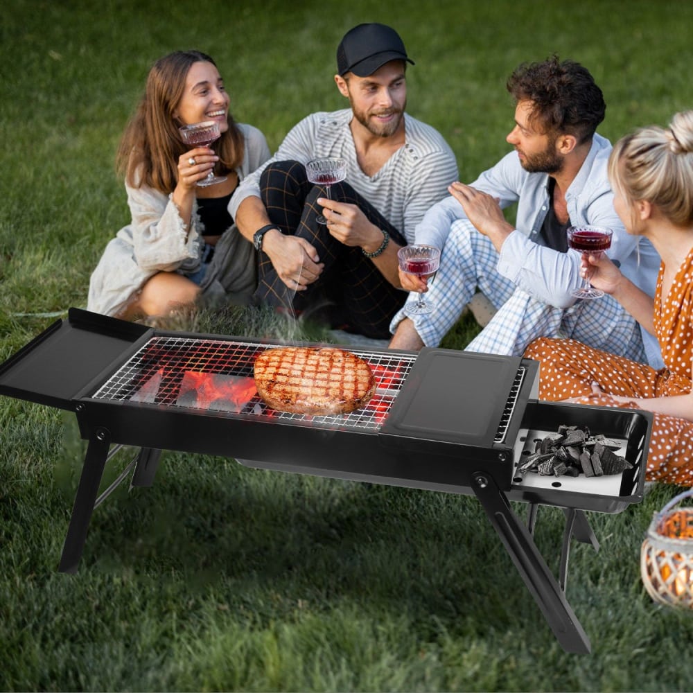 Portable outdoor grill with a perfectly cooked steak, surrounded by friends enjoying wine in a green park setting.